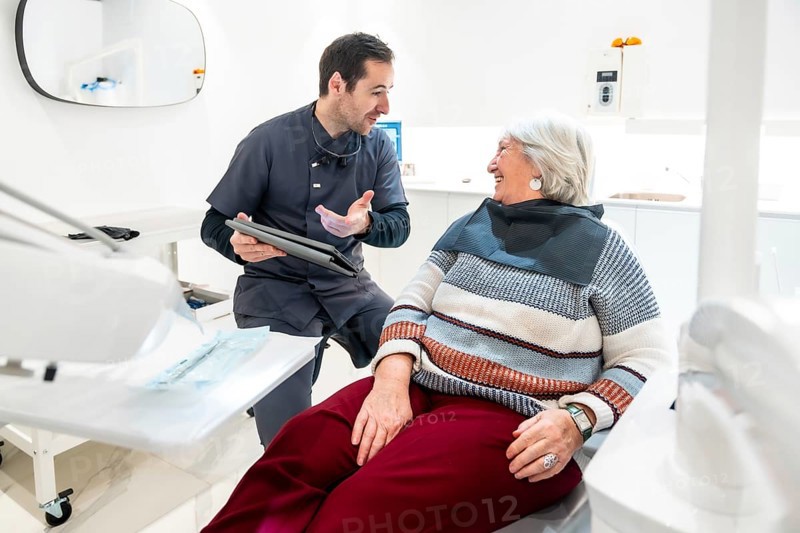 Dentist is explaining something on a tablet to a senior female patient during a consultation in a modern dental clinic
