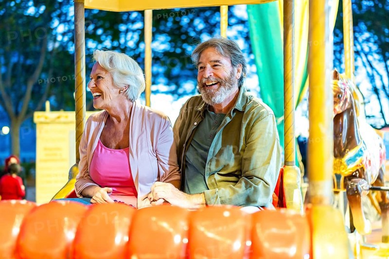 Happy caucasian senior couple enjoying a ride with carousel at night in the city