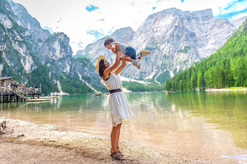 Tourist mother lifting her son in the air while enjoying summer holidays at lake braies, also called pragser wildsee, in the dolomites of italy