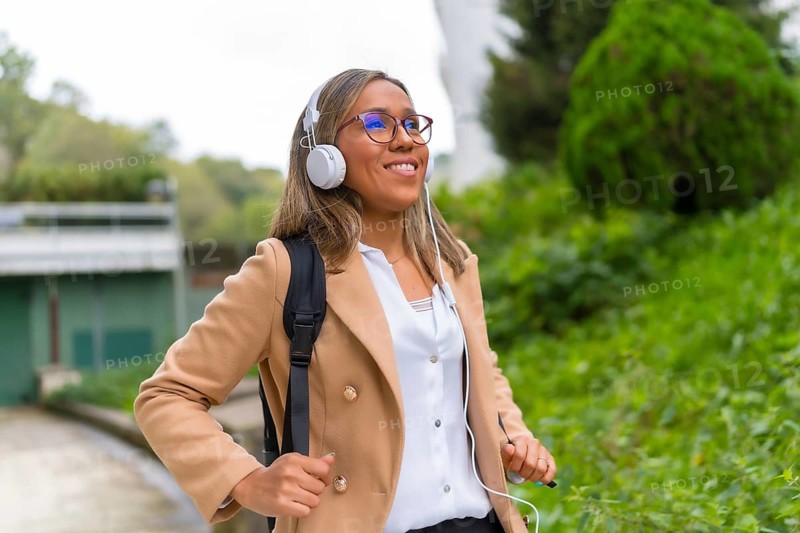 Portrait of a happy latin businesswoman listening to music commuting in the city walking down a residential area