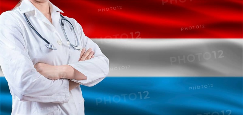 Doctor with crossed arms on Luxembourg flag. Luxembourg health and care concept. Female doctor on Luxembourg flag
