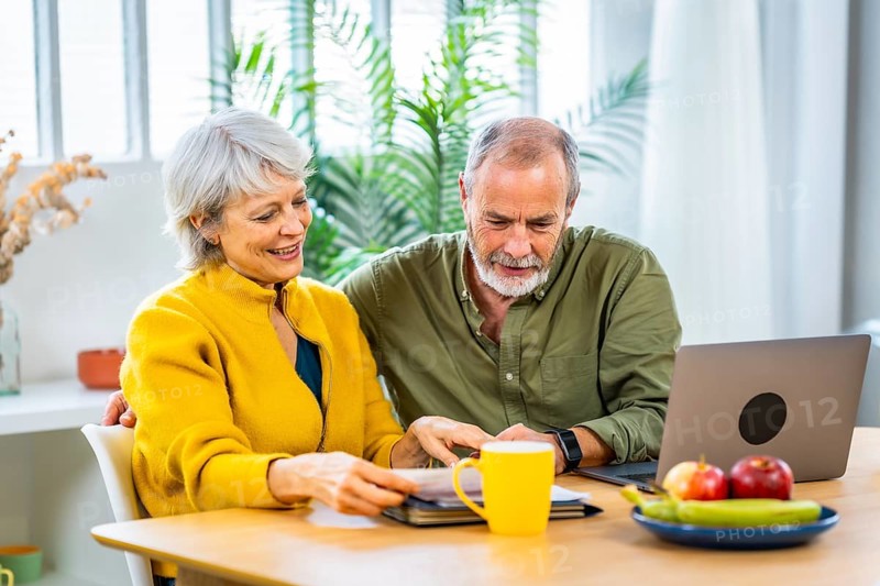 Relaxed senior couple doing paperwork and household accountability together using laptop and drinking coffee
