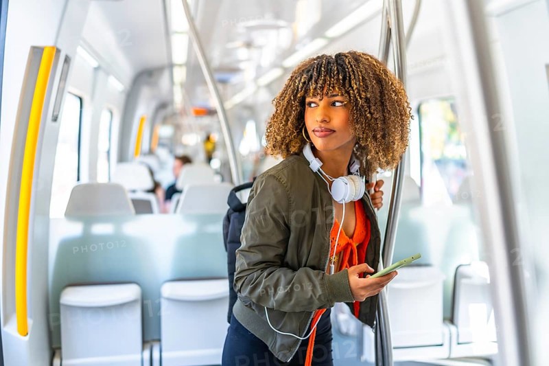 Cool latin woman using phone while looking distracted standing on the train
