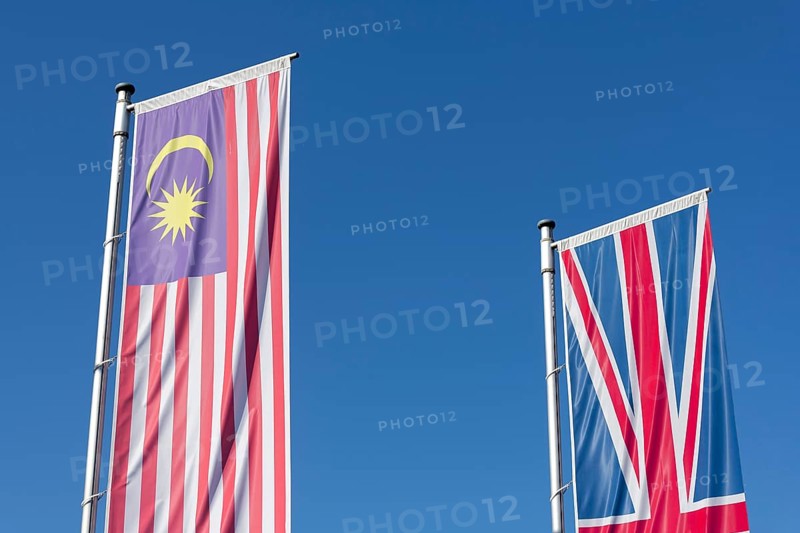 Malaysia and British flags fly against a clear blue sky