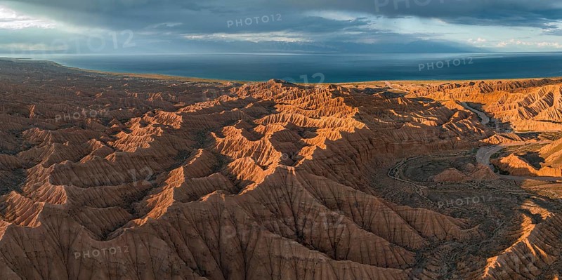 Riverbed runs through a landscape of eroded hills, badlands at sunset, Issyk Kul Lake in the background, aerial view, Canyon of the Forgotten Rivers, Issyk Kul, Kyrgyzstan, Asia