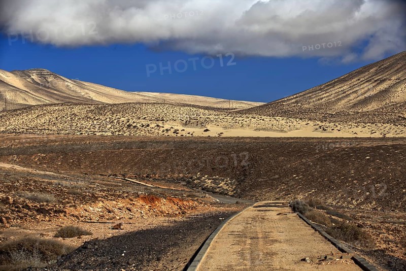Lonely road in front of a dune landscape under a cloudy sky, Pajara, Fuerteventura, Canary Islands, Spain, Europe