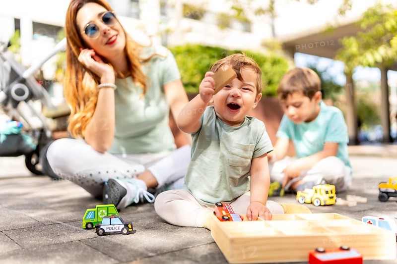 Baby holding a toy and laughing next to his family playing together on an urban park