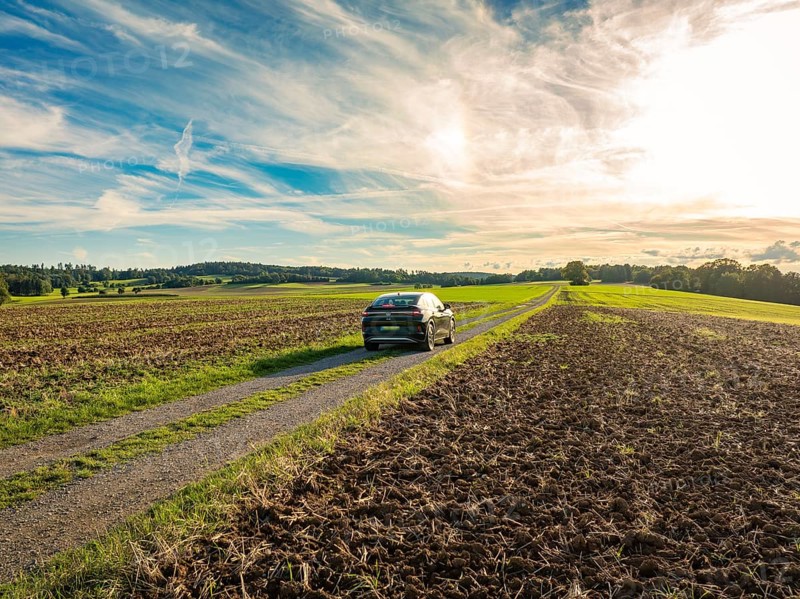 A car drives on a rural road between ploughed fields under a partly cloudy sky, Carsharing, VW ID5, Calw, Black Forest, Germany, Europe