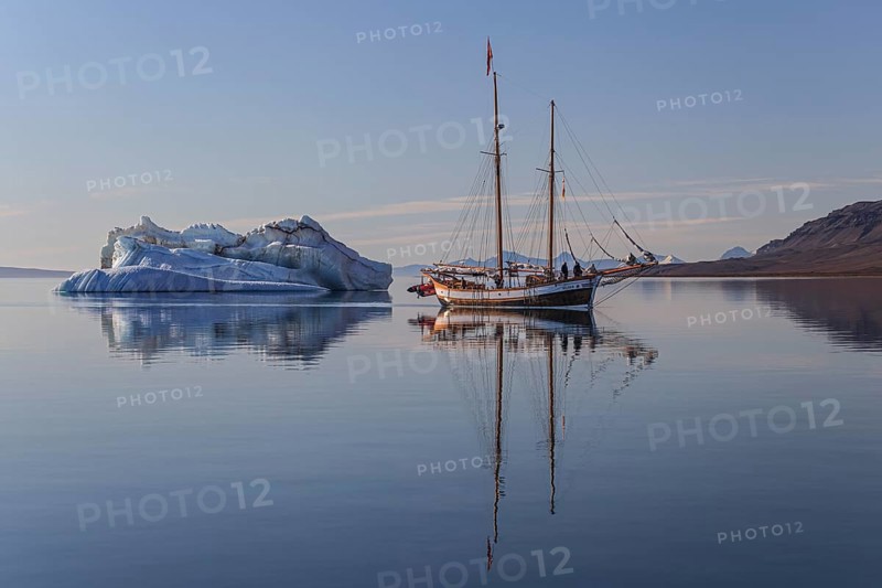 Traditional sailing ship reflected in fjord next to iceberg, sunny, Ittoqqortoormiit, Scoresby Sund, East Greenland, Greenland, North America