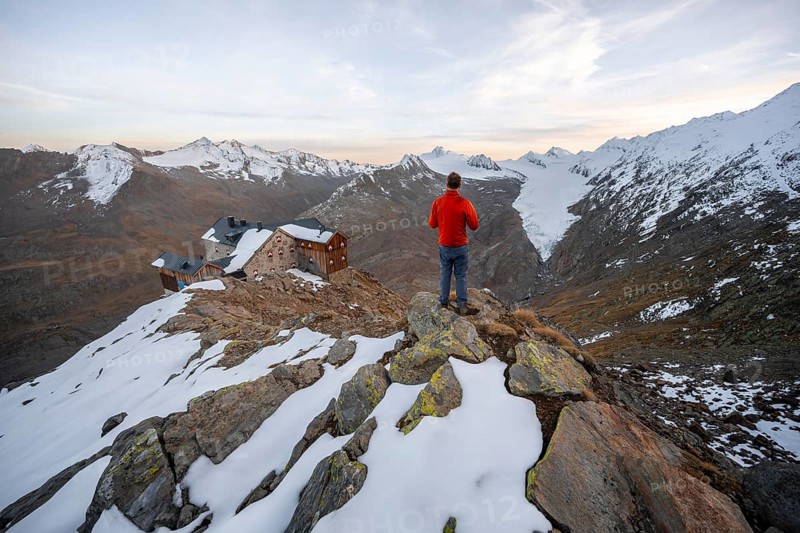 Hiker looking at mountain panorama and glacier, mountain hut Ramolhaus in autumn with snow, at sunset, view of Gurgler Ferner with summit Hochwilde and Falschungsspitze, Ötztal Alps, Tyrol, Austria, Europe