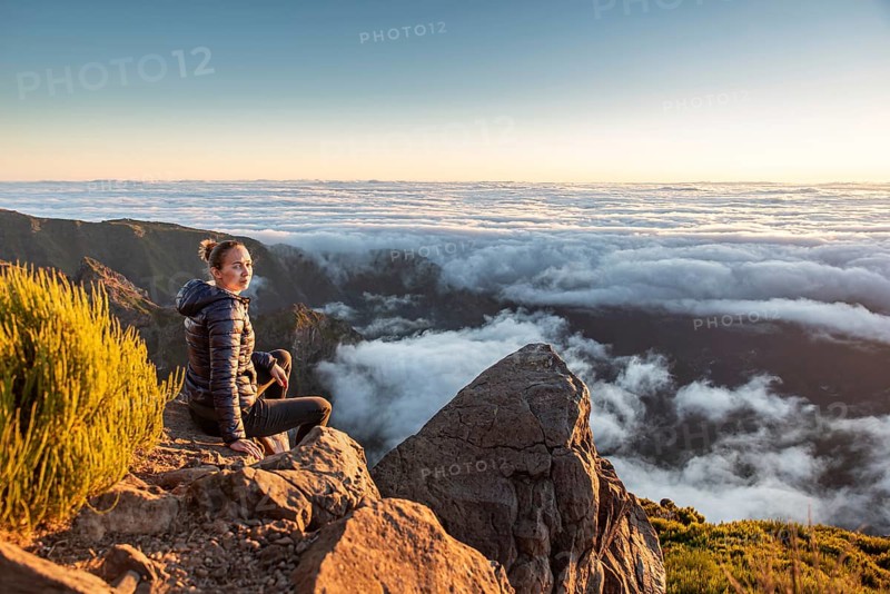 A woman sits on a rocky mountainside and calmly enjoys the wide view over the sea of clouds, Pico Ruivo, Madeira, Portugal, Europe