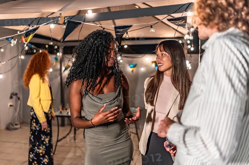 Multi-ethnic young people in elegant clothes chatting during night party at terrace