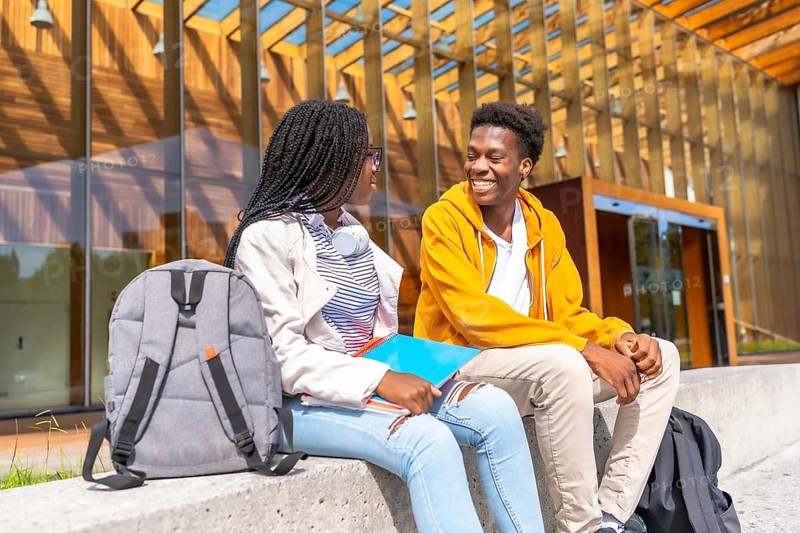 Two male and female african students talking sitting together in the university campus in a sunny day