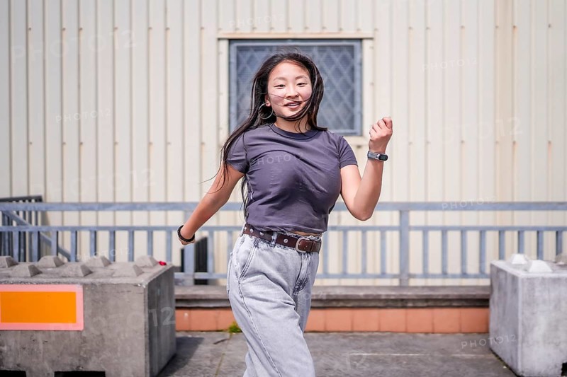 Asian woman dancing energetically k-pop style dance outside an industrial building