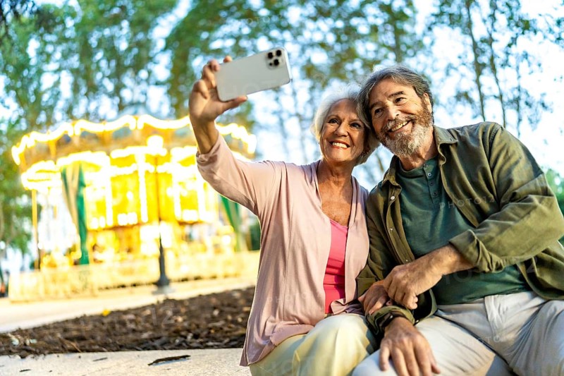 Senior couple taking selfie sitting on bench in a night city fair