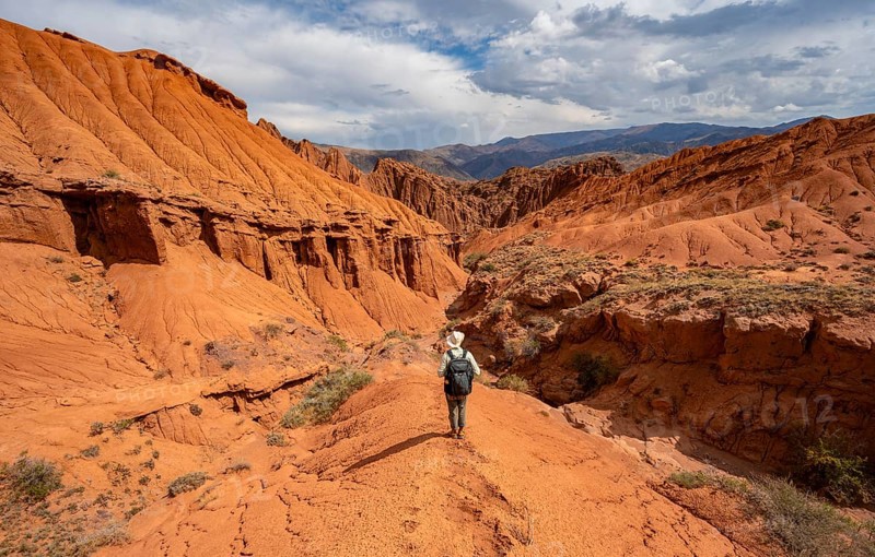 Mountaineer on a mountain ridge, view of eroded mountain landscape with sandstone cliffs, canyon with red and orange rock formations, Konorchek Canyon, Chuy, Kyrgyzstan, Asia