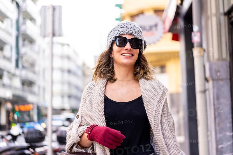 Lifestyle, young Caucasian blonde girl enjoying and smiling in the city in winter. Strolling with sunglasses and red gloves