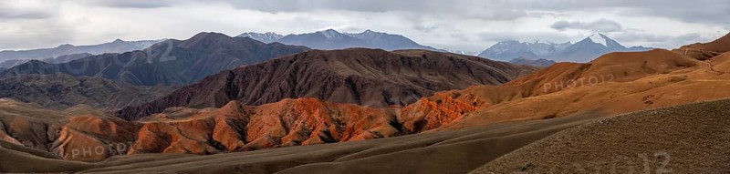 Panorama, view over eroded mountainous landscape of Konorchek Canyon with red sandstone cliffs, high mountains with snow in the background, dramatic dark clouds, Konorchek Canyon, Chuy, Kyrgyzstan, Asia