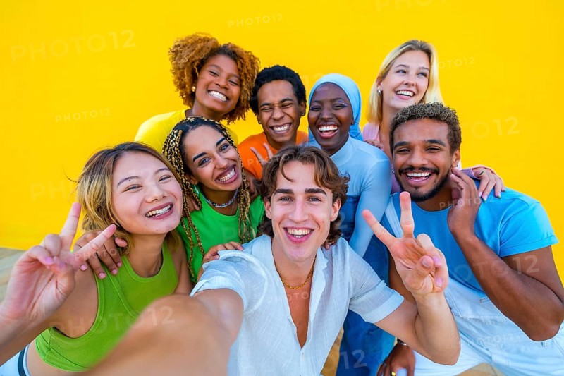 Multi-ethnic friends gesturing success while taking a selfie next to a yellow wall