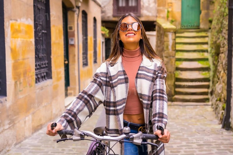 Pretty latin woman with sunglasses doing bicycle sightseeing in the city through the old town. Eco tourism in spring on vacation, model smiling
