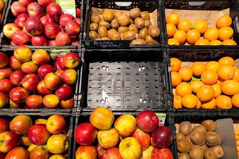 Fruit counter in a supermarket or organic food shop, here with different types of apples, kiwis, oranges and an empty compartment for pears