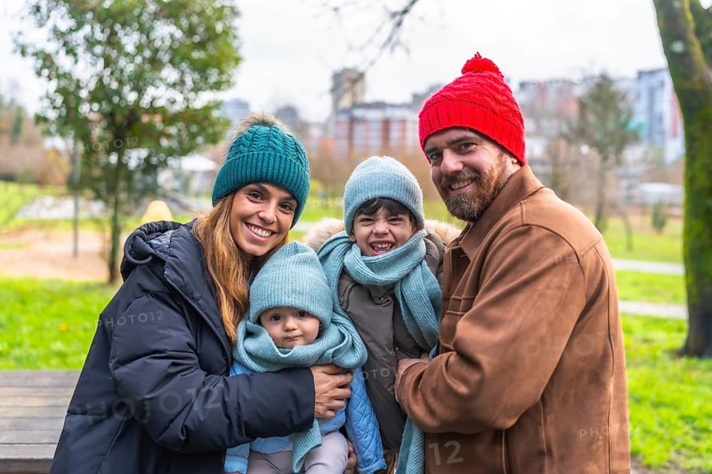 Smiling family bundled in warm winter clothes, enjoying a cheerful day outdoors in a city park, surrounded by nature and joy