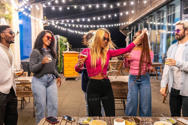 Blonde woman dancing among multi-ethnic friends at night party in a bar terrace in the city