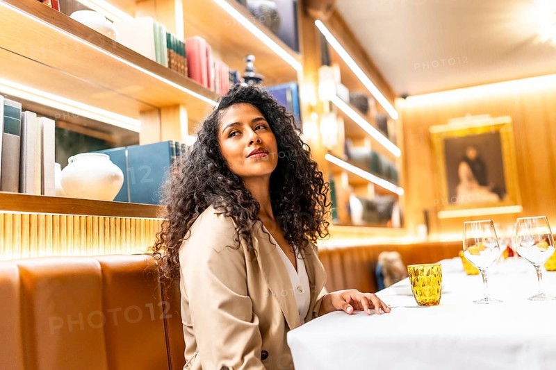 Side view photo of a beauty chic latin woman sitting distracted in a restaurant looking aside alone
