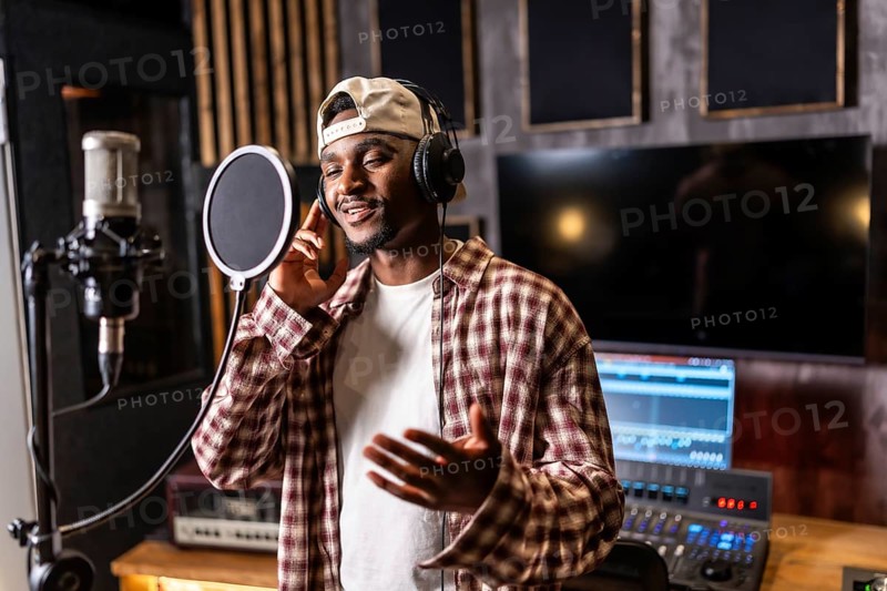 Young happy african american male singer wearing headphones and singing in professional recording studio