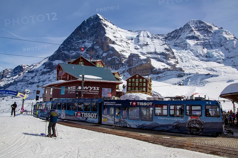 25 March 2024, Kleine Scheidegg, Grindelwald Switzerland : Many skiers and tourists enjoy the sunny winter weather. In the background the famous north face of the Eiger, in the foreground the Wengernalp railway, the longest cog railway in the world