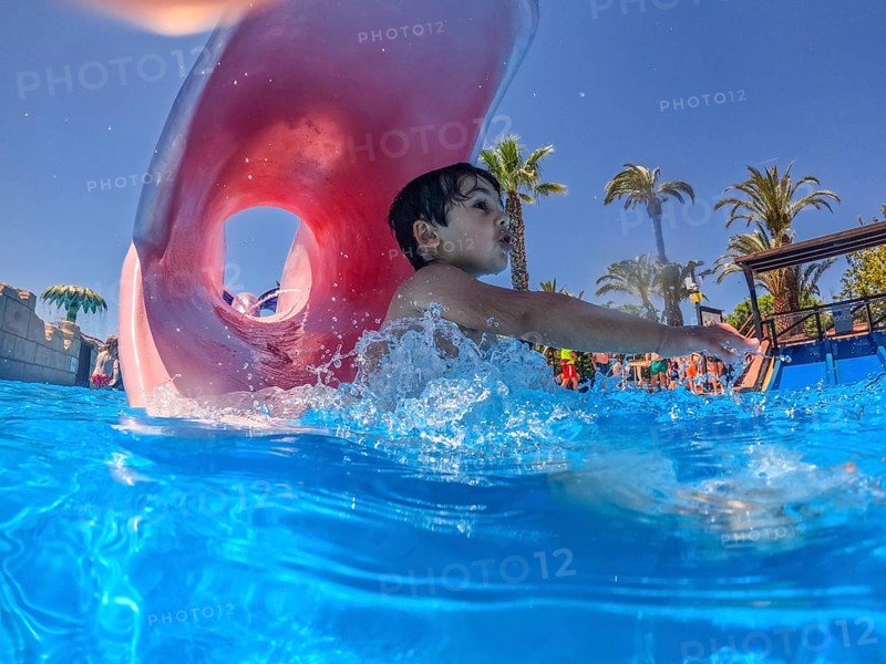 Young boy sliding joyfully into a pool at a vibrant water park, delighting in the excitement of summer vacation and playful splashes