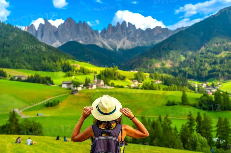Female tourist holding her hat while looking at st. Magdalena church in val di funes with the odle mountains in the background