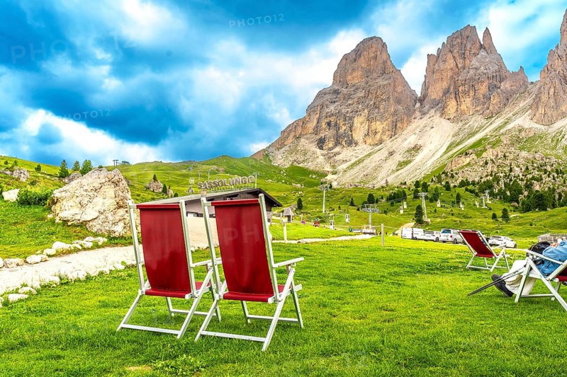 Red deckchairs inviting tourists to relax and enjoy the breathtaking view of the sassolungo mountain in the dolomites during summer