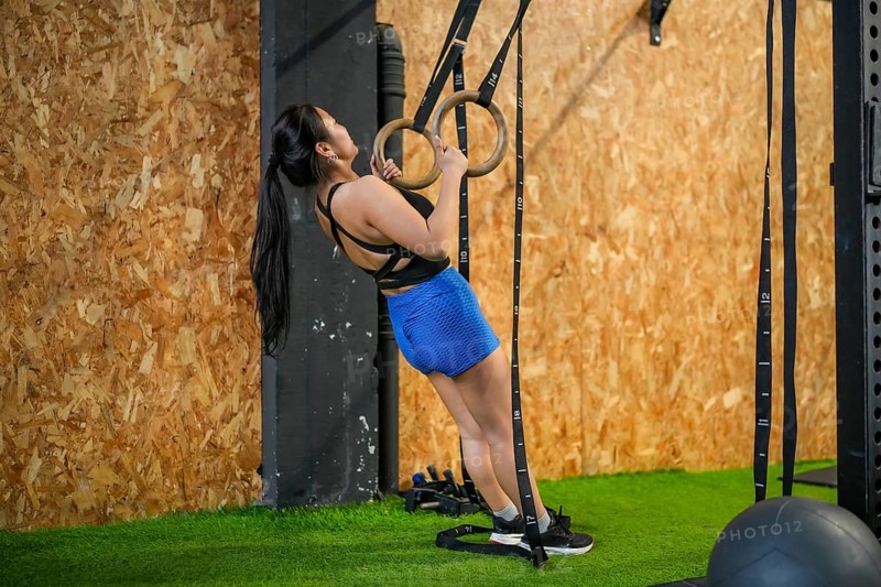 Full length side view of an asian woman exercising using gym rings to do pull-ups