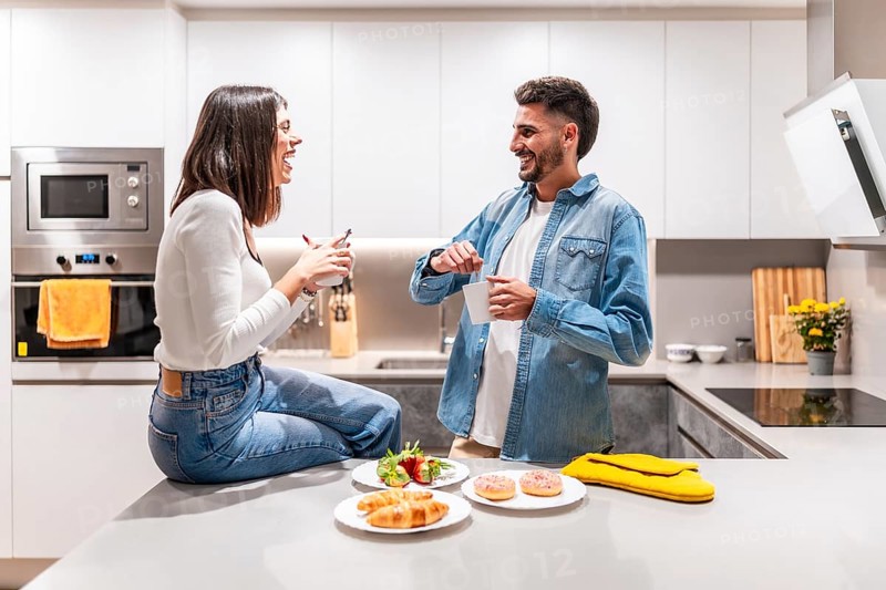 Young couple laughing and talking while having breakfast and coffee in their modern kitchen