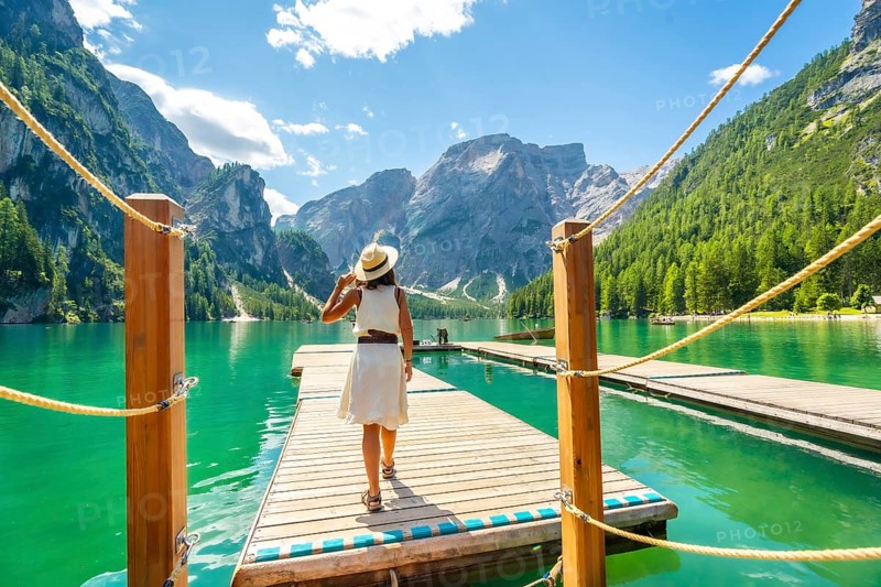 Woman walking along a wooden pier at lake braies, enjoying the turquoise waters and stunning mountain landscape of the dolomites on a sunny summer day