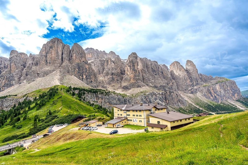 Green meadows and a mountain hotel are surrounded by the breathtaking peaks of the dolomites on a sunny summer day
