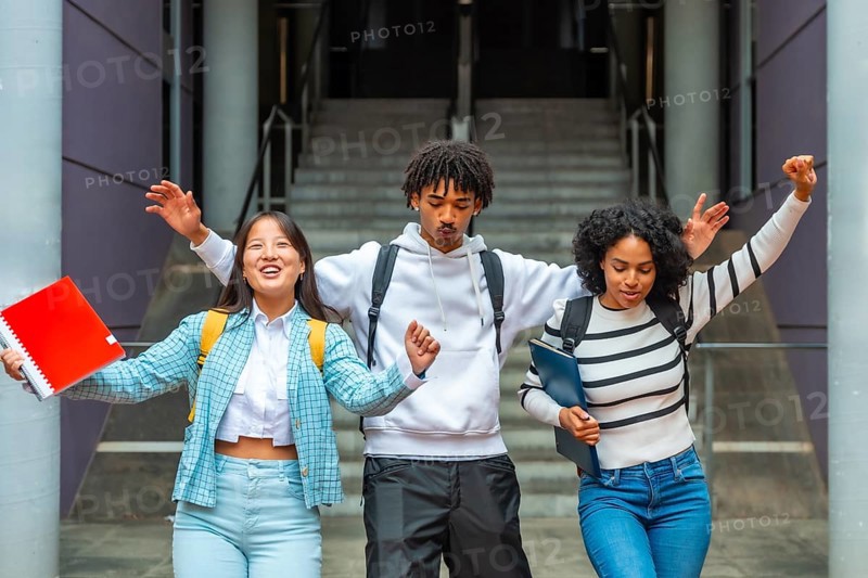 Three multi-ethnic female and male students having fun celebrating and dancing outside the university