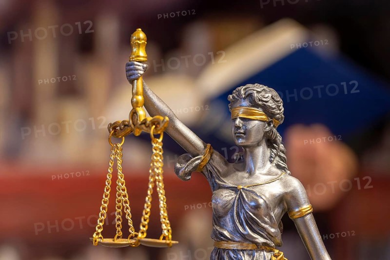 Close-up of a Justitia, in the background a man is reading a book (symbolic image)