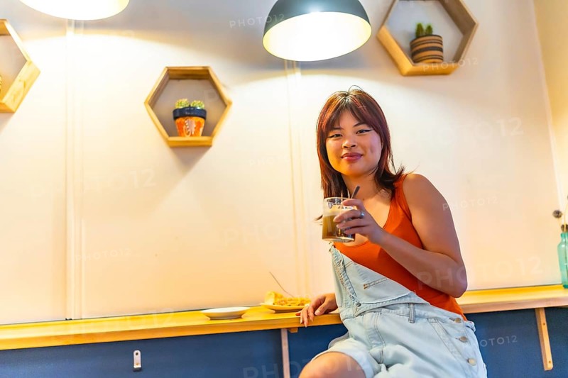 Low angle view portrait of an asian cool young woman smiling at camera sitting drinking coffee in a cafeteria