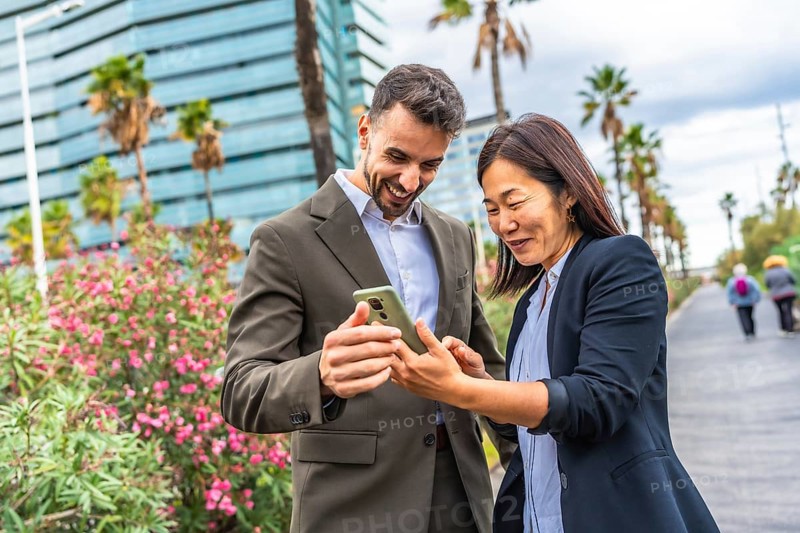 Happy multi-ethnic business people using mobile and smile standing in a financial district in a tropical city