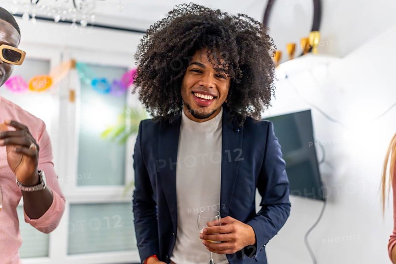 Latin cheerful man with curly hair smiling at camera during home party with friends