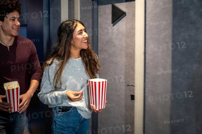 Happy couple walking into a movie theater, holding popcorn buckets and tickets, excited for the show