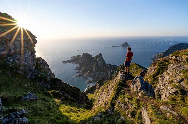 Mountaineer on the summit of Måtind or Måtinden, view of picturesque coastal landscape with sun star, rocky coast and sea, Andøya Island, Vesterålen, Nordland, Norway, Europe