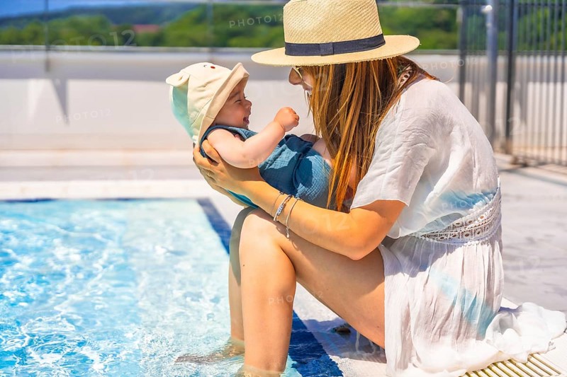Side view of a mother and cute baby with sun hat in the swimming pool