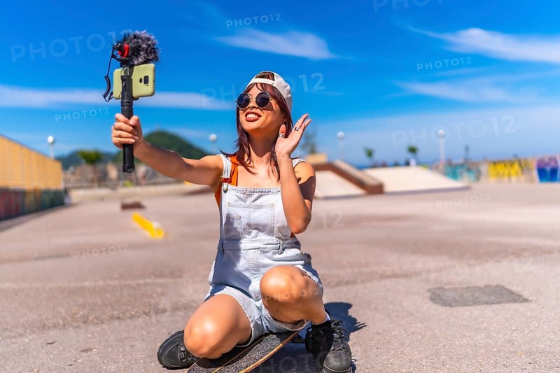 Asian young woman are doing livestreaming joyfully in skateboard urban park waving at the camera while recording