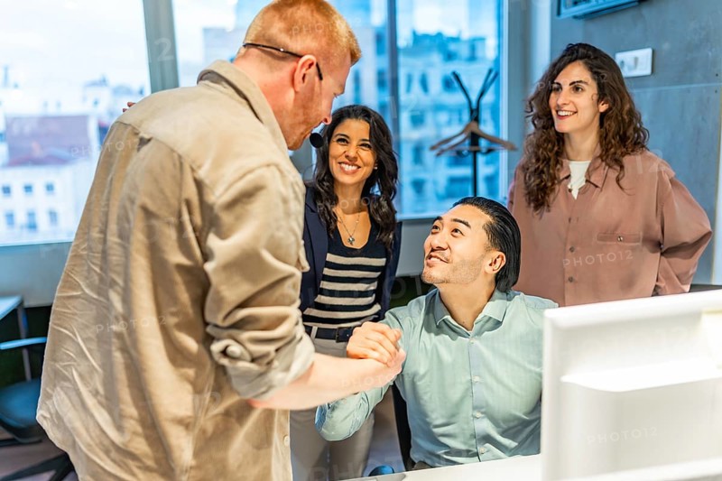 Business team congratulating their colleague on a successful project, shaking hands in the office workplace