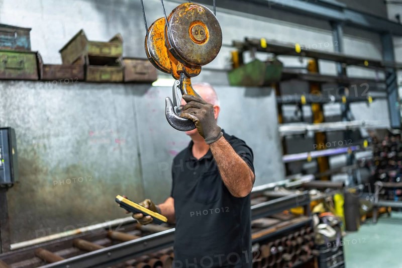 Mature caucasian man holding the hook of an industrial crane while operating in a factory