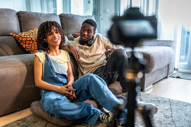 Two influencers are recording a vlog in their living room, discussing lifestyle and fashion tips for their online audience