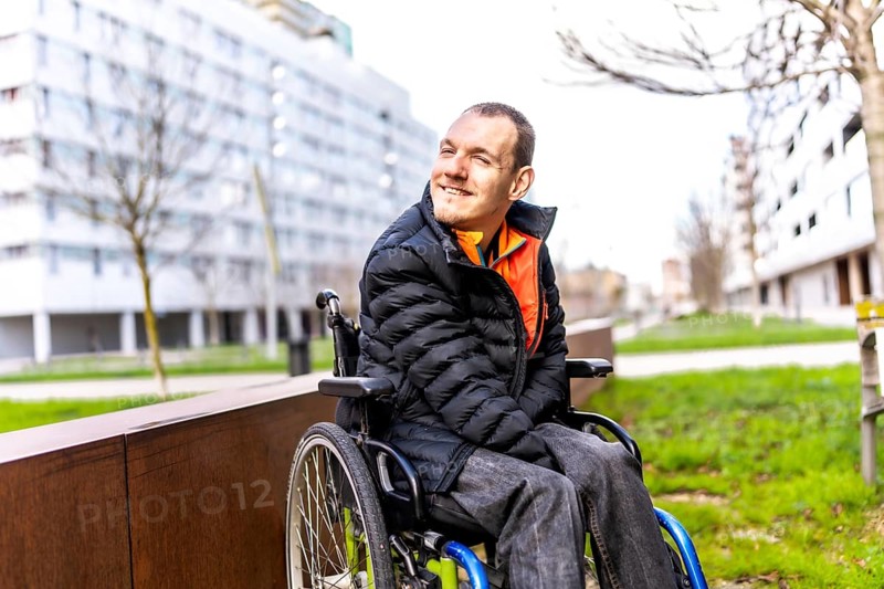 Young man using wheelchair smiling while enjoying a day out in an urban park, promoting inclusion and accessibility